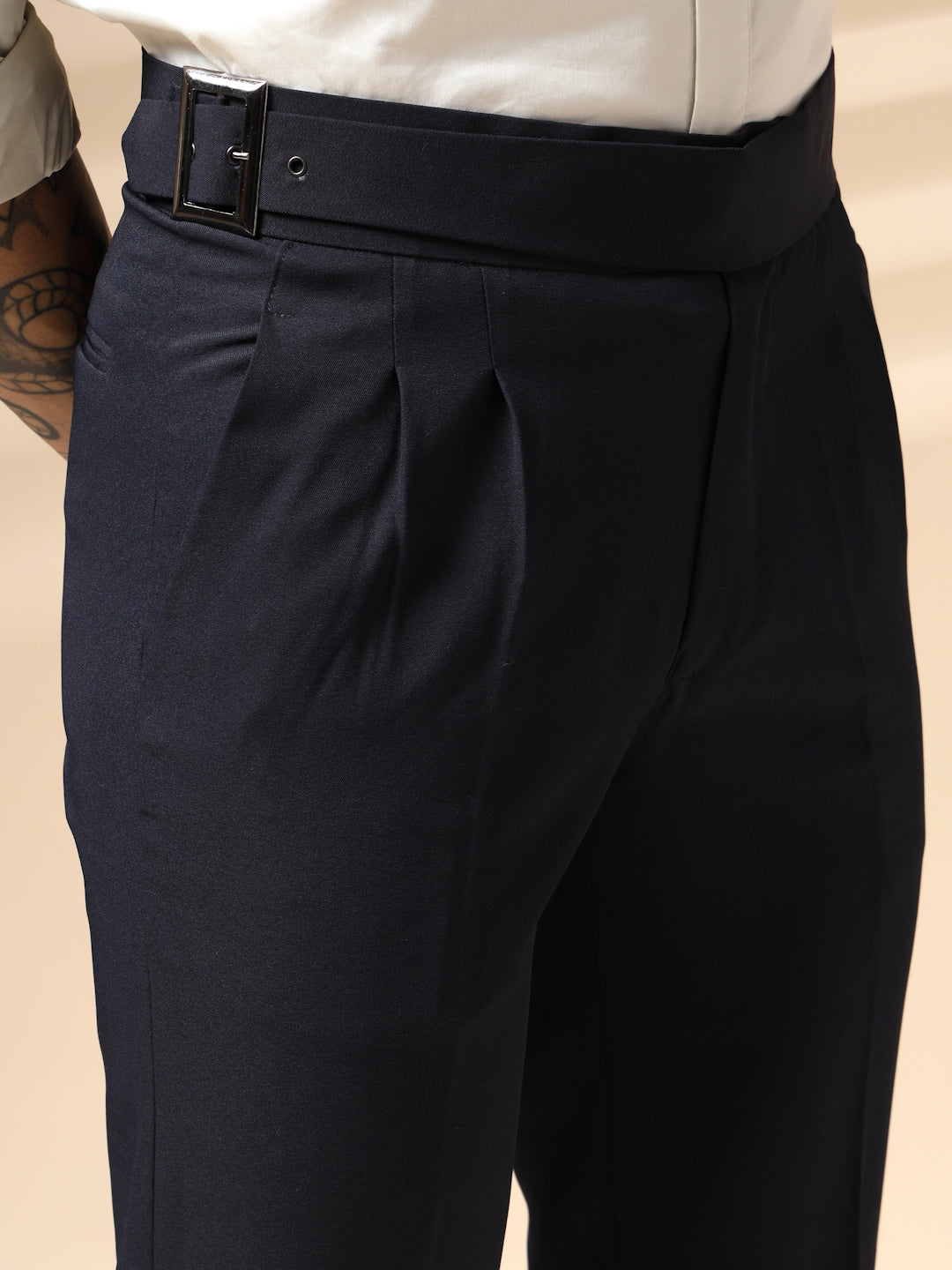 Black pleated Gurkha Pant with a belt on a beige background